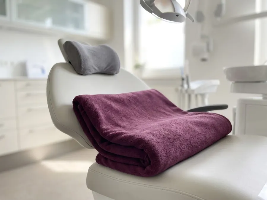 A soft blanket and head rest pillow on a dental chair.